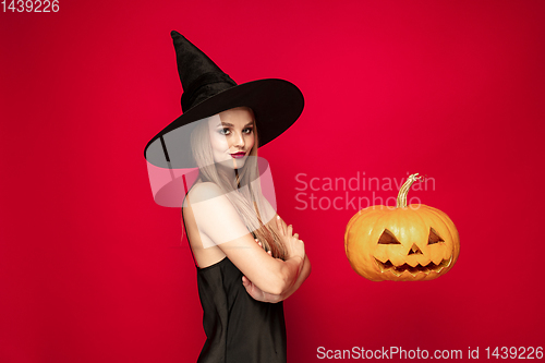 Image of Young woman in hat as a witch on red background