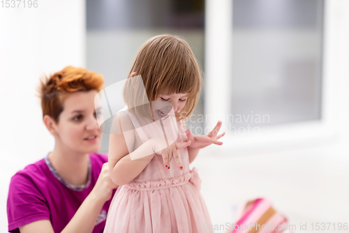 Image of young mother helping daughter while putting on a dress