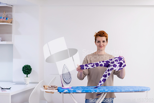 Image of Red haired woman ironing clothes at home