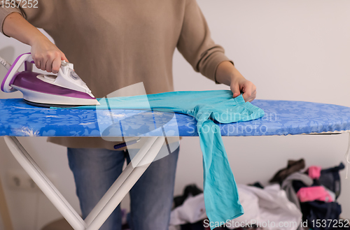 Image of Red haired woman ironing clothes at home