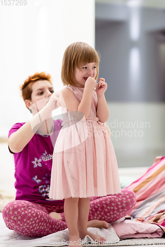 Image of young mother helping daughter while putting on a dress