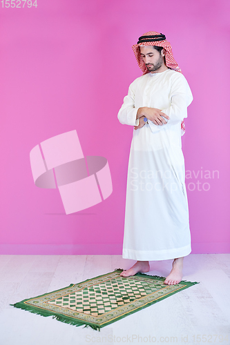 Image of young arabian muslim man praying on the floor at home