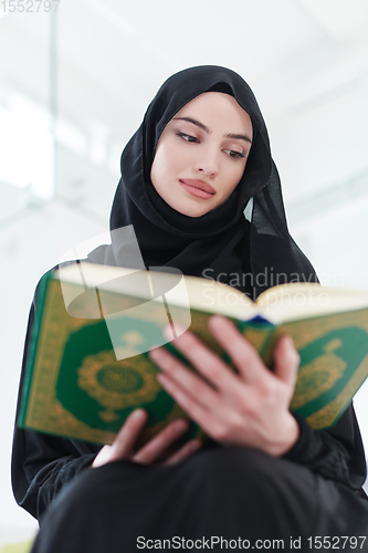 Image of young muslim woman reading Quran at home