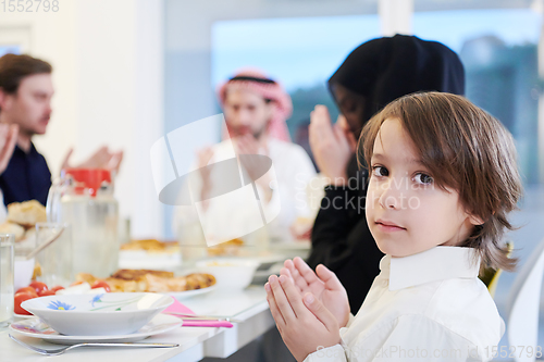 Image of little muslim boy praying with family before iftar dinner