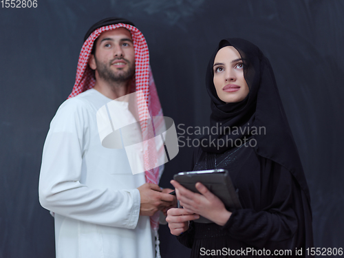 Image of muslim couple using modern technology in front of black chalkboa