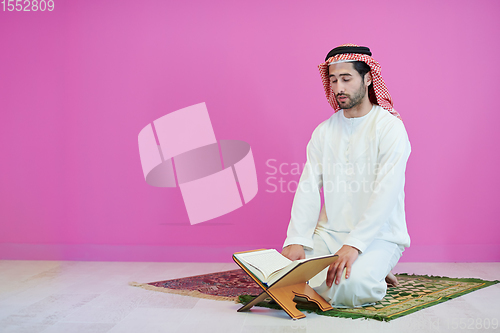 Image of young arabian muslim man reading Quran at home