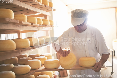 Image of Cheese maker at the storage with shelves full of cow and goat cheese