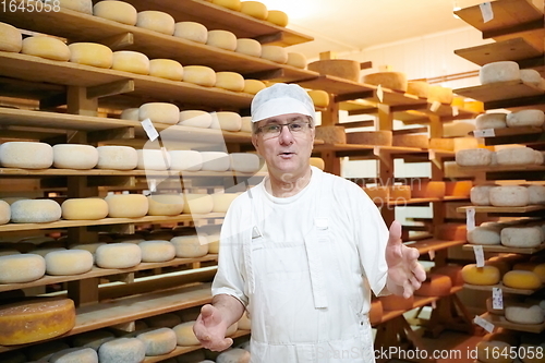 Image of Cheese maker at the storage with shelves full of cow and goat cheese