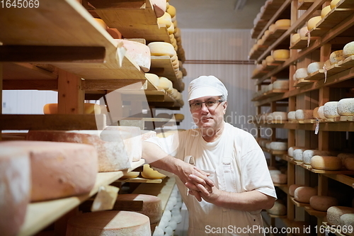 Image of Cheese maker at the storage with shelves full of cow and goat cheese