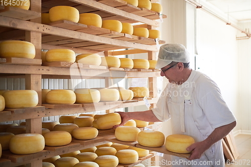 Image of Cheese maker at the storage with shelves full of cow and goat cheese