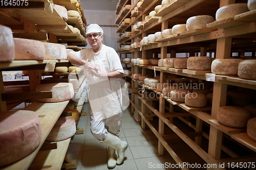 Image of Cheese maker at the storage with shelves full of cow and goat cheese