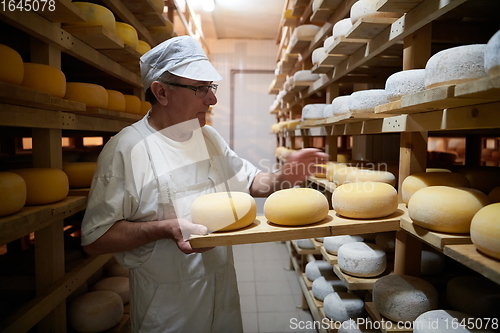 Image of Cheese maker at the storage with shelves full of cow and goat cheese