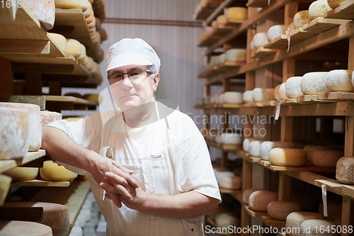 Image of Cheese maker at the storage with shelves full of cow and goat cheese