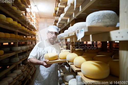 Image of Cheese maker at the storage with shelves full of cow and goat cheese