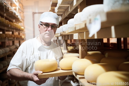 Image of Cheese maker at the storage with shelves full of cow and goat cheese