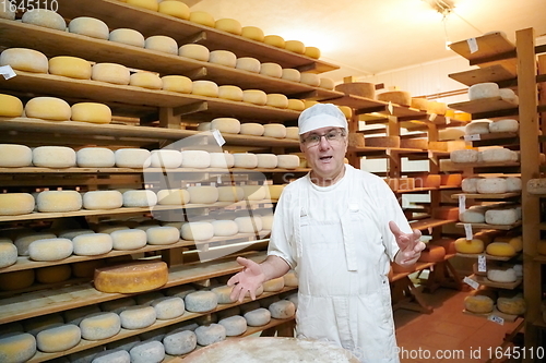 Image of Cheese maker at the storage with shelves full of cow and goat cheese