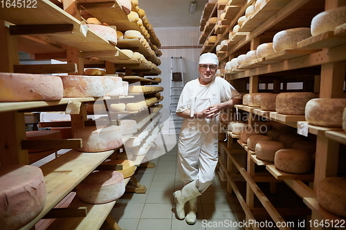Image of Cheese maker at the storage with shelves full of cow and goat cheese