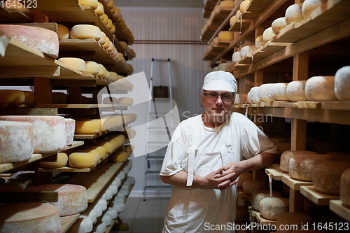 Image of Cheese maker at the storage with shelves full of cow and goat cheese