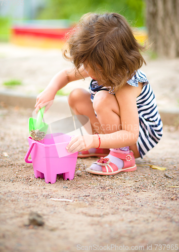 Image of Little girl is playing with sand in playground