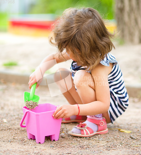 Image of Little girl is playing with sand in playground