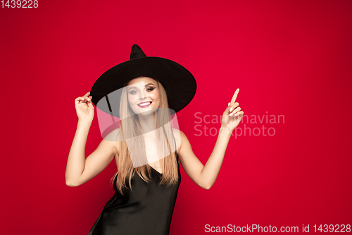 Image of Young woman in hat as a witch on red background