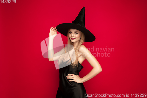 Image of Young woman in hat as a witch on red background