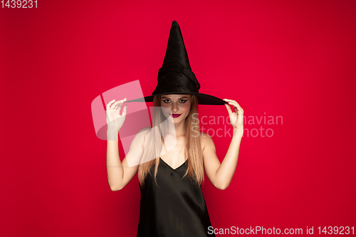 Image of Young woman in hat as a witch on red background