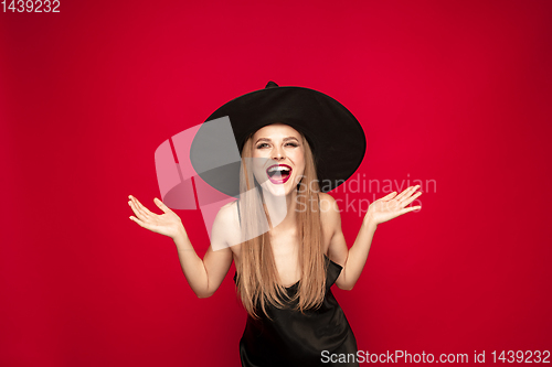 Image of Young woman in hat as a witch on red background