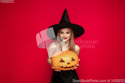 Image of Young woman in hat as a witch on red background