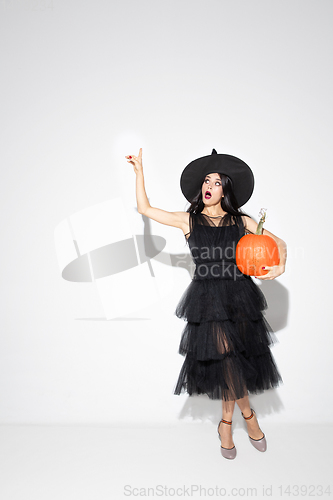 Image of Young woman in hat and dress as a witch on white background