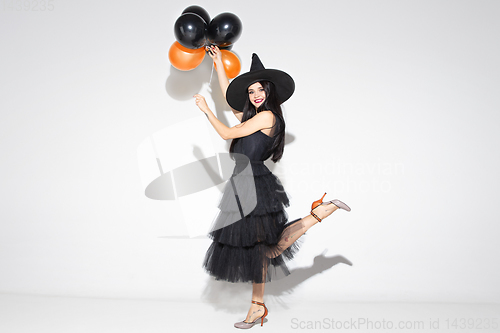 Image of Young woman in hat and dress as a witch on white background