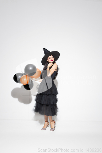 Image of Young woman in hat and dress as a witch on white background