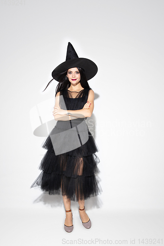 Image of Young woman in hat and dress as a witch on white background