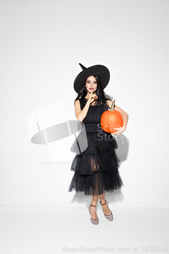 Image of Young woman in hat and dress as a witch on white background