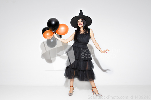 Image of Young woman in hat and dress as a witch on white background