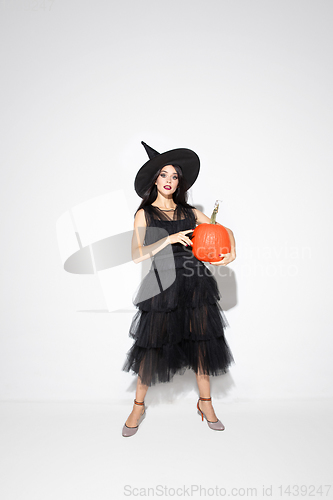 Image of Young woman in hat and dress as a witch on white background