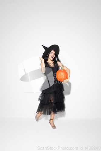 Image of Young woman in hat and dress as a witch on white background