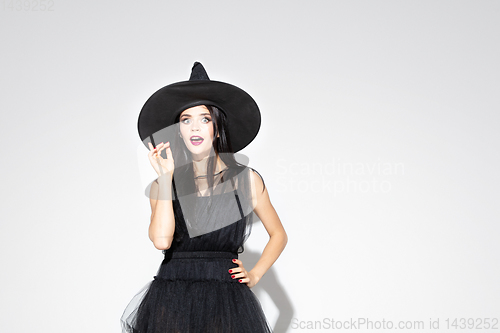 Image of Young woman in hat and dress as a witch on white background