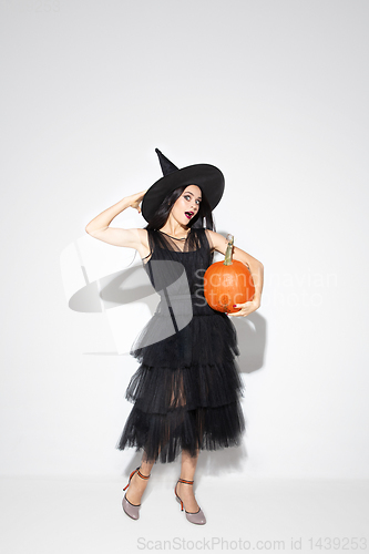 Image of Young woman in hat and dress as a witch on white background