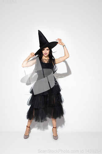 Image of Young woman in hat and dress as a witch on white background