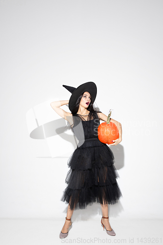 Image of Young woman in hat and dress as a witch on white background