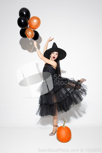 Image of Young woman in hat and dress as a witch on white background