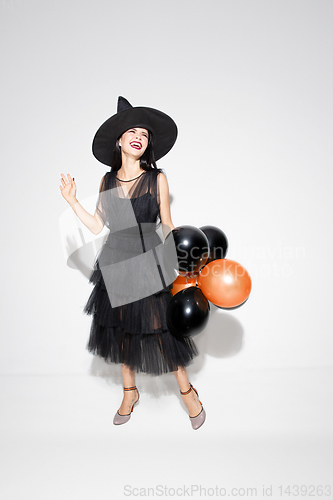 Image of Young woman in hat and dress as a witch on white background