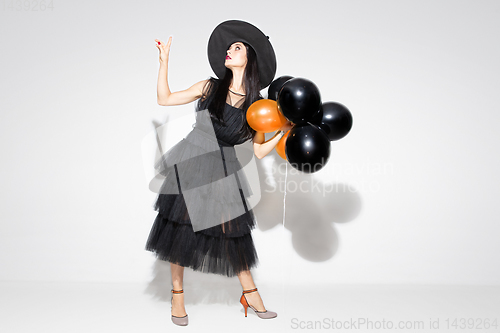 Image of Young woman in hat and dress as a witch on white background