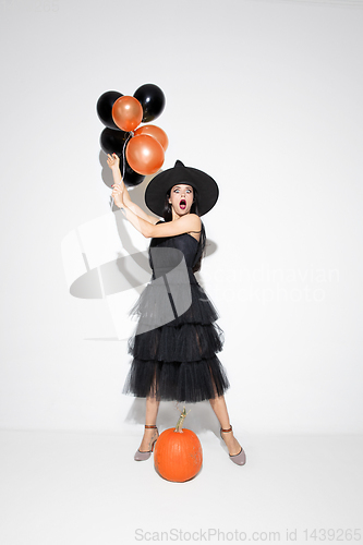 Image of Young woman in hat and dress as a witch on white background