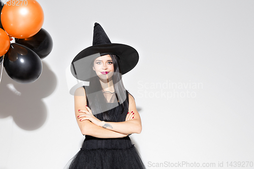 Image of Young woman in hat and dress as a witch on white background