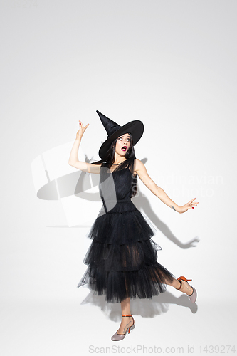 Image of Young woman in hat and dress as a witch on white background
