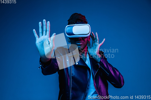 Image of Young african-american woman\'s using VR-glasses in neon light