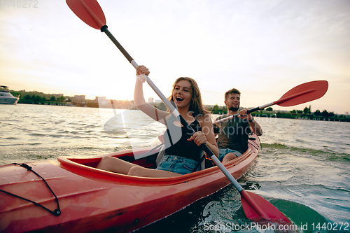 Image of Confident young couple kayaking on river together with sunset on the background