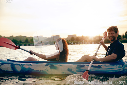 Image of Confident young couple kayaking on river together with sunset on the background